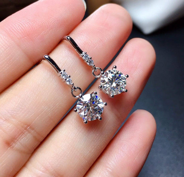 One carat moissanite diamond earrings in sterling silver with original design held in hand